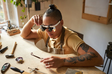Portrait of artisanal jeweler with tattoes working on art piece at wooden tableの写真素材