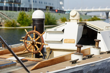 Background image of small yacht in sunlight, focus on wooden steering wheel, copy space