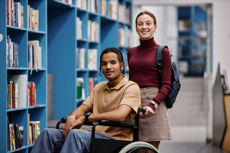 Portrait of smiling young woman assisting student with disability in library both looking at camera