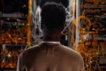 Back view of black young man as system administrator looking at servers, copy spaceの写真素材