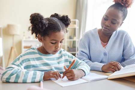 Portrait of cute black girl studying at home with caring mother or tutor helping