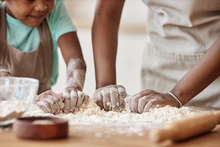 Close up of mother and daughter baking together in kitchen and kneading dough for homemade pastry