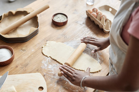 Close up of black woman baking homemade pastry and rolling dough on wooden kitchen counter, copy...
