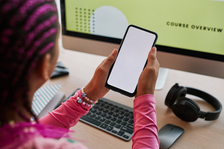High angle closeup of black teenage girl using smartphone with blank screen at desk, copy spaceの写真素材
