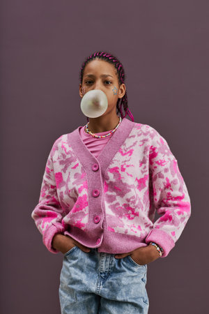 Vertical waist up portrait of black teenage girl blowing bubblegum bubble while looking at camera in...
