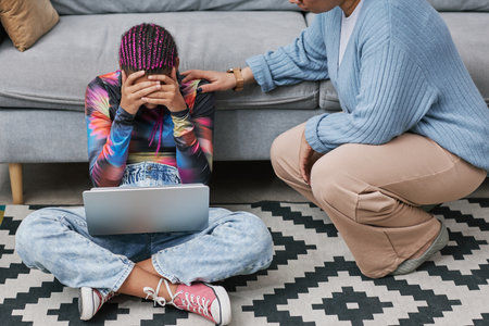 Full length portrait of depressed teenage girl sitting on floor with mother or therapist trying to communicateの写真素材