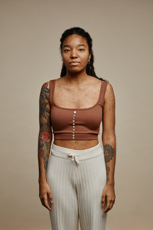 Minimal portrait of young black woman looking at camera standing against neutral beige background with focus on real skin texture with spots and acne scarsの写真素材