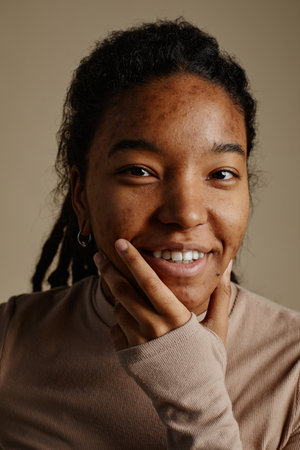 Close up portrait of young black woman smiling genuinely and looking at camera in neutral tones