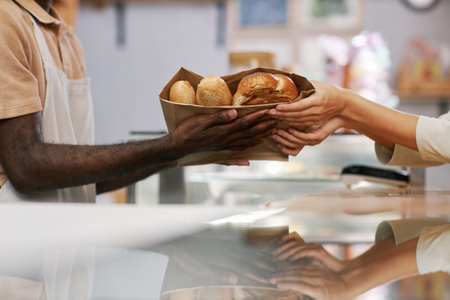 Hands of bakery cashier giving package of fresh bread to customer