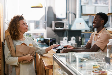 Happy woman using contactless payment app when paying for bread in local bakery