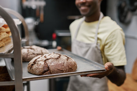 Closeup image of smiling baker putting tray with freshly baked bread in bakers rackの写真素材