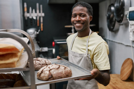 Portrait of positive baker holding tray with fresh rye breadの写真素材