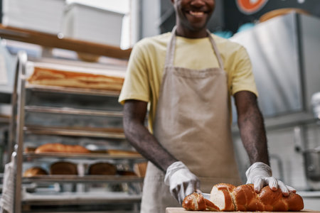 Smiling baker cutting braided bread with poppy seeds for customerの写真素材
