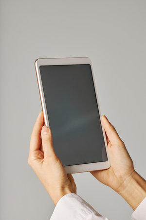 Vertical closeup of female hand holding tablet with blank screen against white backgroundの写真素材