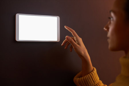 Closeup of young woman using digital control panel with blank screen on wall at homeの写真素材