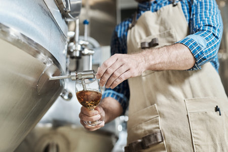 Close up of unrecognizable male brewmaster pouring glass of beer at brewing factoryの写真素材