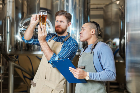 Waist up portrait of brewmaster holding beer glass while inspecting quality of production at brewing factory, copy spaceの写真素材
