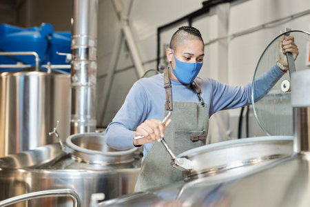 Portrait of female worker wearing mask opening tanks at beer making factoryの写真素材
