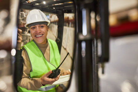 Portrait of smiling young woman wearing hardhat while operating forklift truck in warehouse, copy spaceの写真素材