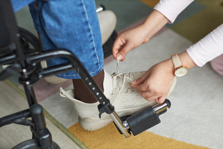 Close-up of young woman helping man with disability to tie shoelace on his shoe