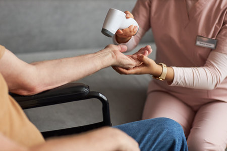 Close-up of caregiver in uniform holding arm of senior man and checking temperature with special...