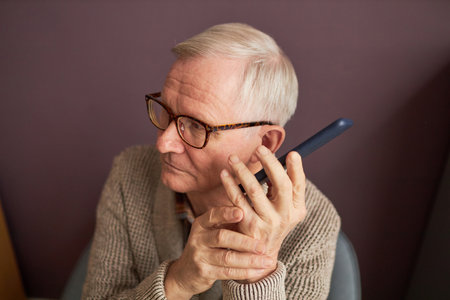 Blind man with gray hair in eyeglasses listening to audio on his mobile phoneの写真素材