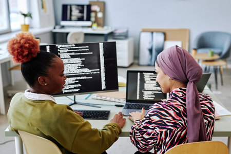 Back view at two female programmers writing code and discussing project together