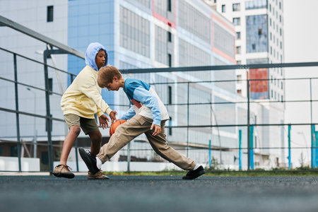 Two adolescent intercultural schoolboys in activewear playing basketball on playground while trying to hold the ball during sports gameの写真素材