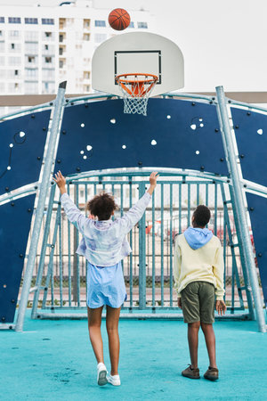 Back view of two African American schoolkids playing basketball while standing on playground and throwing ball into basketの写真素材
