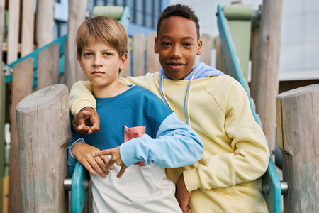 Two youthful intercultural buddies in casualwear looking at camera while standing by wooden...