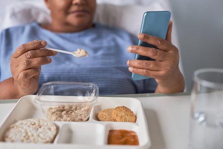 Close up of black senior woman eating healthy meal on tray in hospital recovery room, copy spaceの写真素材