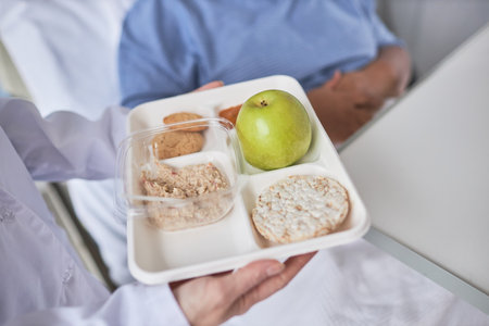 Close up of nurse holding healthy breakfast meal on tray and bringing in to patient in hospitalの写真素材