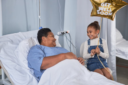 Portrait of black little girl visiting grandma in hospital room and holding balloons