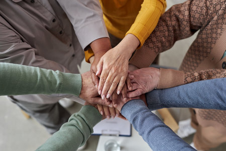 Top view closeup of senior people stacking hands in circle during support group session in retirement homeの写真素材
