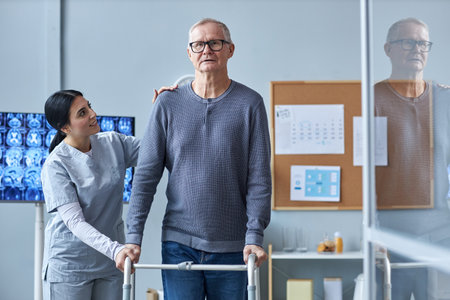 Waist up portrait of smiling nurse assisting senior man using mobility walker in retirement homeの写真素材