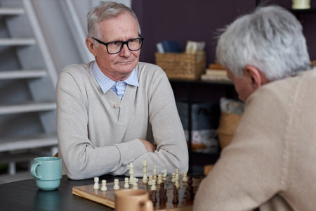 Portrait of two senior people playing chess in common room area at retirement home