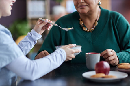 Close up of young caring nurse feeding senior woman with spoon at retirement home or assisted living facilityの写真素材