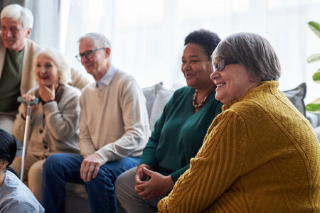 Side view at group of smiling senior people watching TV while sitting in row in retirement home...