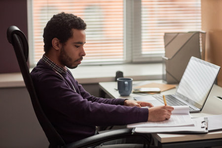 Side view portrait of young man working with documents at desk in office against windowの写真素材
