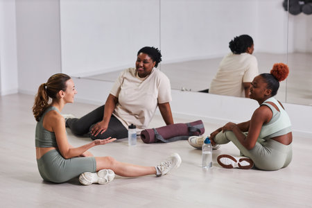Young women sitting on the floor and talking to instructor about training in gymの写真素材