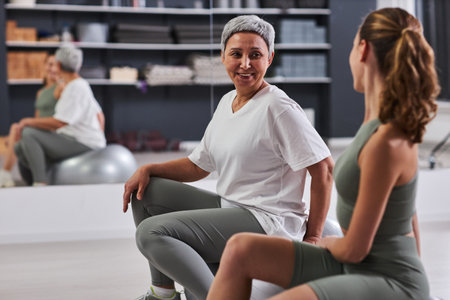 Mature woman exercising on fitness ball together with instructor in health clubの写真素材