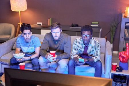 High angle view at group of friends watching TV at home and eating snacks lit by blue light