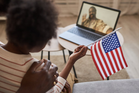 Rear view of child with american flag supporting her mom during war service, they talking online on laptop together with dadの写真素材