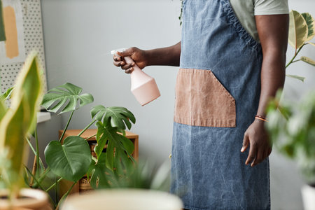 Side view close up of unrecognizable black man watering plants indoors while caring for greenery at home, copy spaceの写真素材