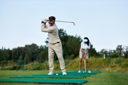 Full length portrait of sporty man playing golf outdoors and swinging club while standing on platformの写真素材