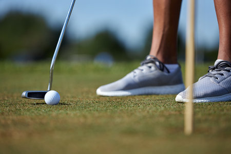 Closeup of unrecognizable person playing golf with focus on golf club hitting ball on grass, copy spaceの写真素材