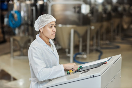 Side view portrait of female worker wearing lab coat using control panel at food factory, copy spaceの写真素材