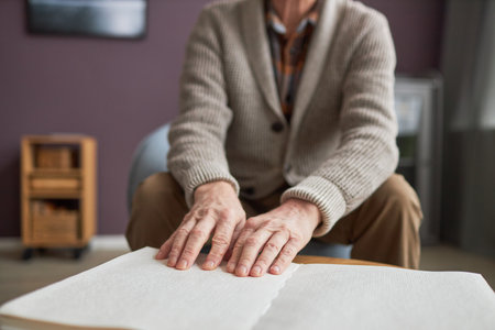 Close-up of senior man with disability reading a book in Braille at table during his leisure time at homeの写真素材