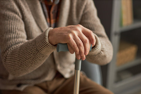Close-up of senior man in jumper with stick sitting on sofa in the roomの写真素材