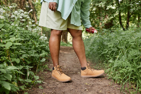Low section shot of black woman spaying legs with bug repellant standing in grass and travelling in...